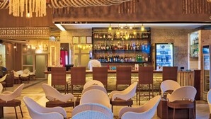 Un coin bar avec des chaises en osier, un barman et une étagère bien garnie de bouteilles.