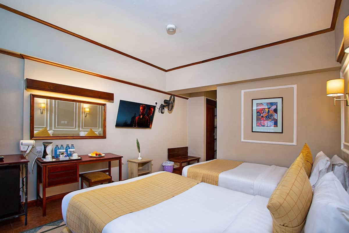 A hotel room with two beds, a desk with a chair, a mirror, and a small table with a lamp.