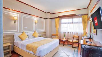 A hotel room with a bed, a desk, a chair, a TV, and a window with curtains.
