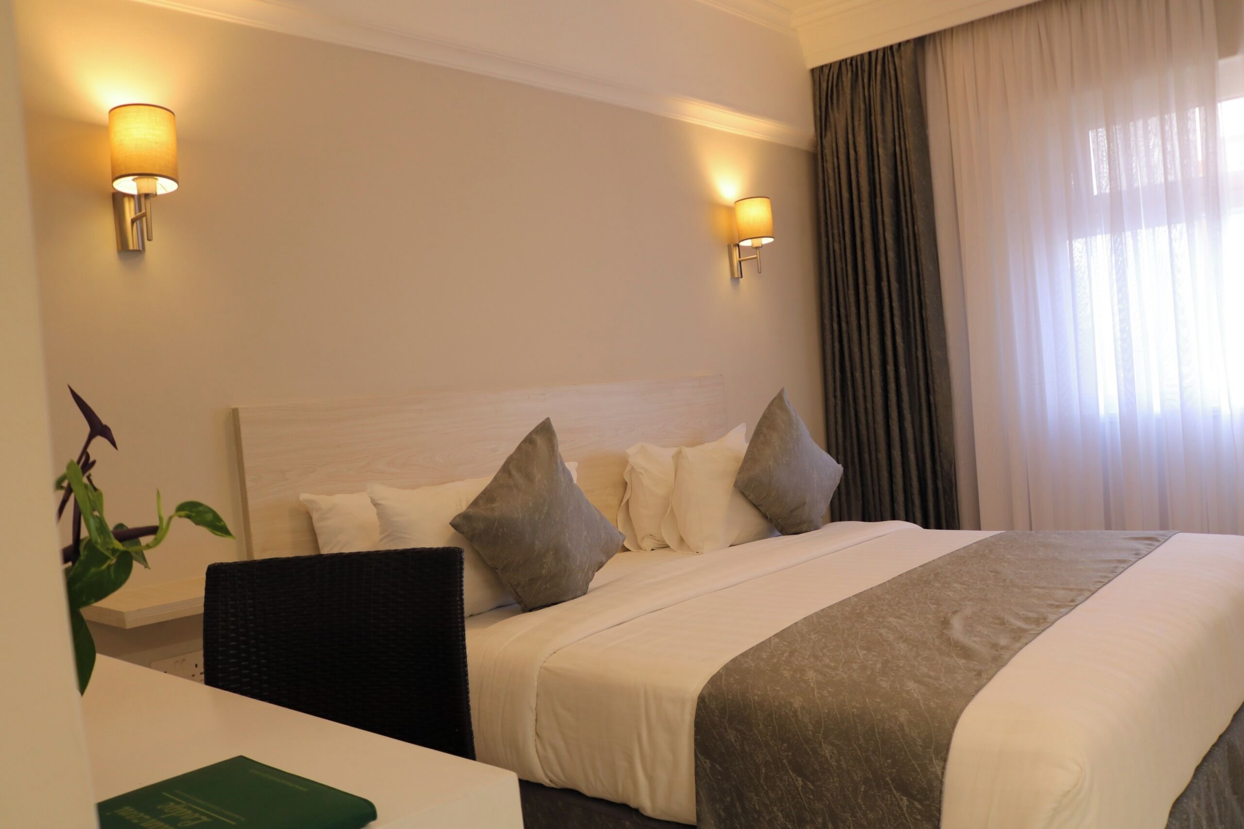 Habitación de hotel con una cama grande, dos lámparas de noche, un escritorio con una silla y una planta.