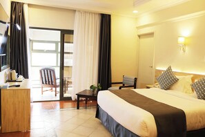 A hotel room with a bed, a desk, a chair, a table with a plant, and a view of the outside. - Maanzoni 680 hotel (Nairobi)