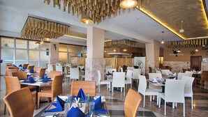 Un restaurant spacieux avec de hauts plafonds, un éclairage moderne et un mélange de chaises en osier et de chaises blanches.