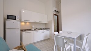 Une cuisine moderne avec des meubles blancs, un four à micro-ondes et une machine à café. On y trouve également un coin repas avec une table et des chaises blanches.