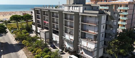 A multi-story hotel with balconies, located near a beach.