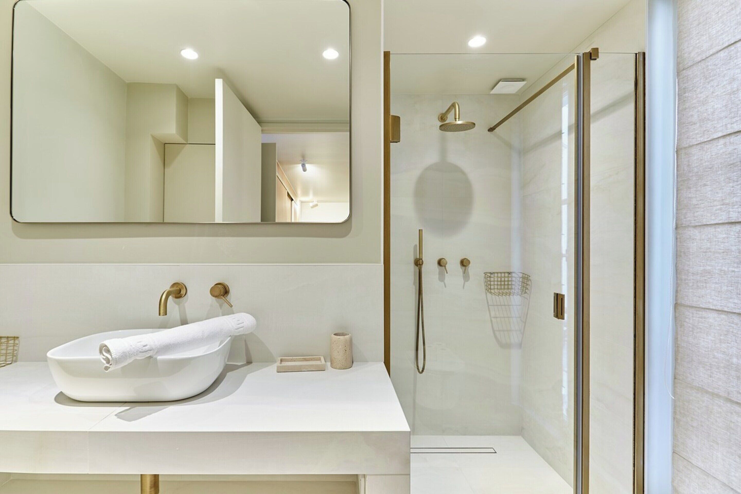 Une salle de bain moderne avec un lavabo blanc, des robinetteries dorées et une douche à parois de verre.