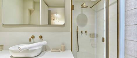 Une salle de bain moderne avec un lavabo blanc, des robinetteries dorées et une douche à parois de verre.