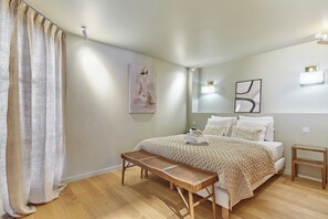 Une chambre à coucher comprenant un lit, un banc, une table de chevet et un luminaire fixé au mur.