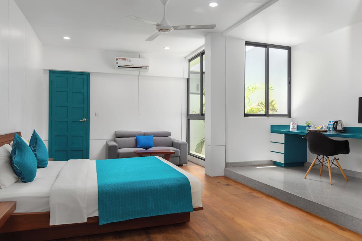 A modern bedroom with a bed, a gray sofa, a desk, and a window.