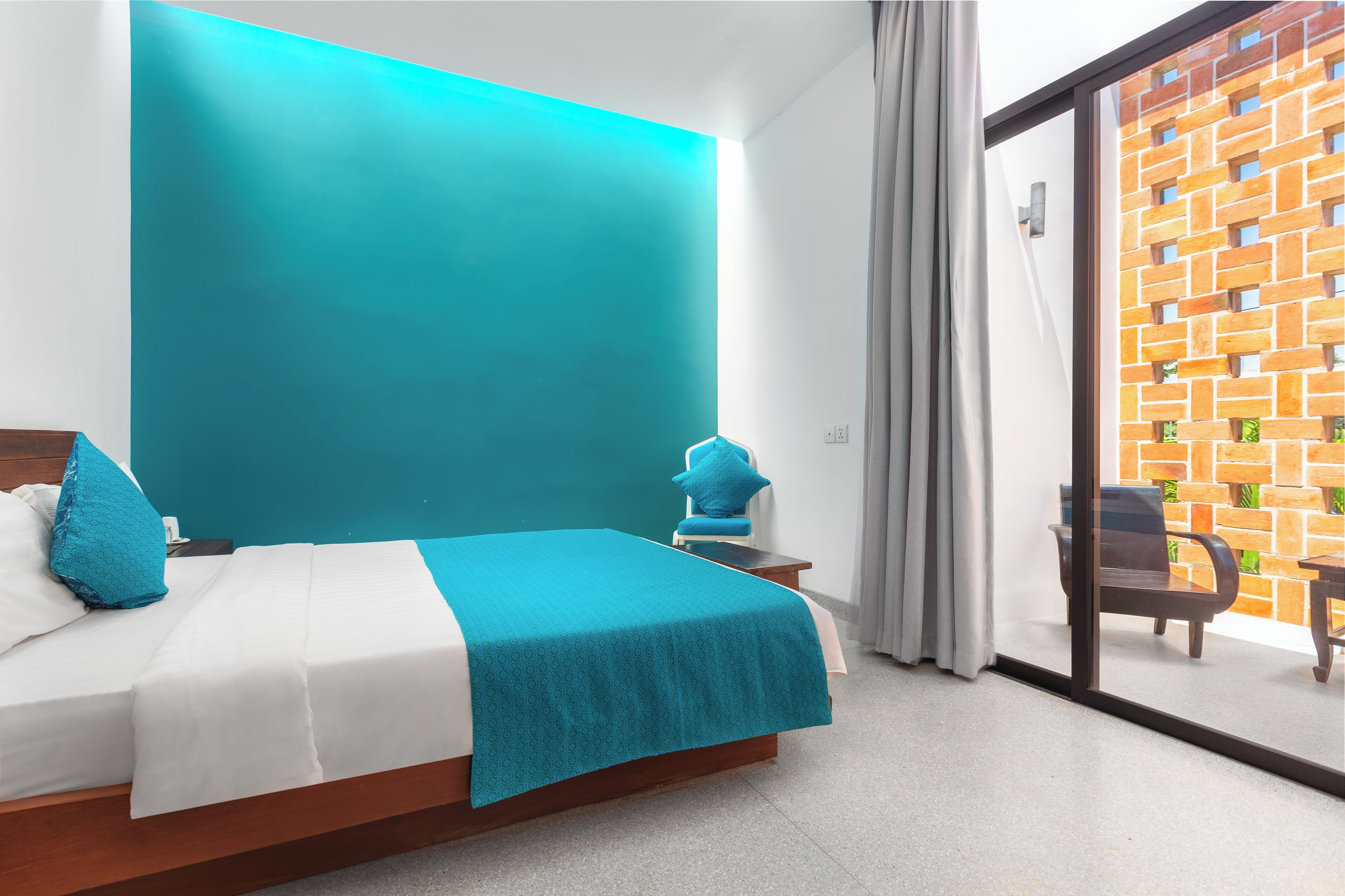 Une chambre d’hôtel avec un lit, une table de chevet, une chaise et une vue sur un mur de briques, visible à travers une porte vitrée.