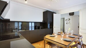 A modern kitchen with a central island, dark cabinetry, and a dining area with a wooden table set for four. - Sublime Apartment With AC Louvre Museum (Paris)