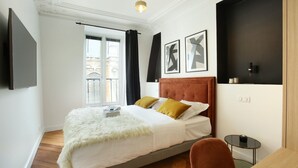 A modern hotel room with a large bed, a small table, a TV mounted on the wall, and a window with curtains. - Sublime Apartment With AC Louvre Museum (Paris)