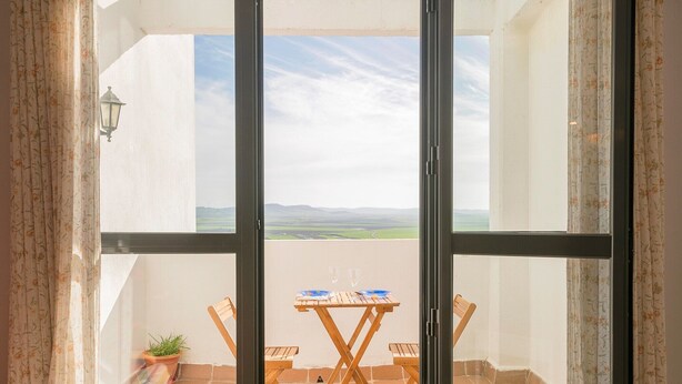 Een balkon met een tafel en stoelen, een bloempot en uitzicht op het landschap.