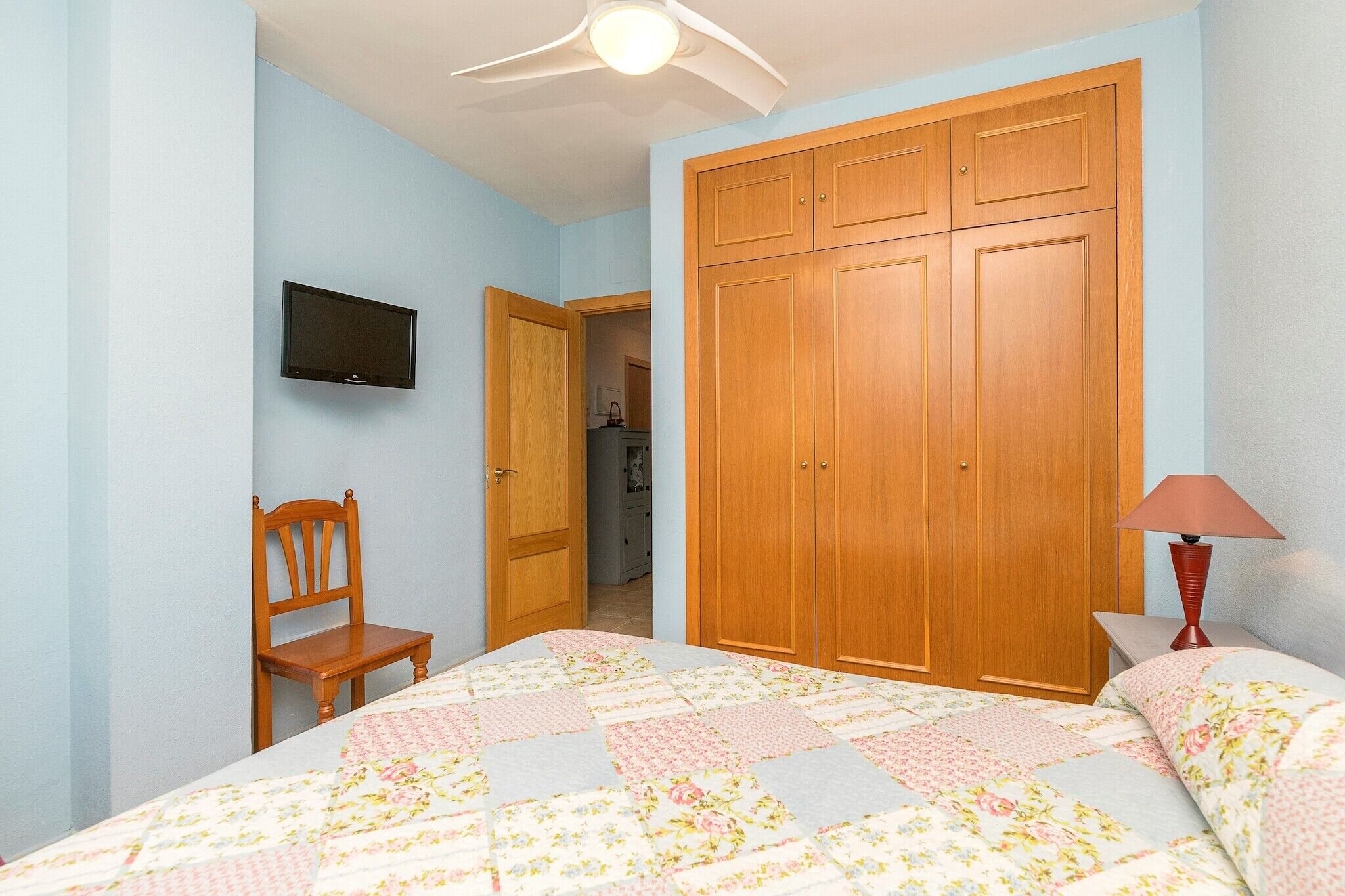 Ein Schlafzimmer mit einem Bett, einem Holzschrank, einem Fernseher und einem Sessel.