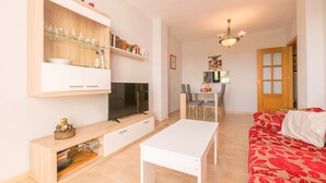 Een moderne woonkamer met een televisie, een witte tafel, een rode bank en een eethoek met stoelen en een tafel.