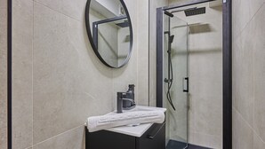 Un baño moderno con un espejo redondo, un lavamanos blanco y una ducha con mampara de vidrio.