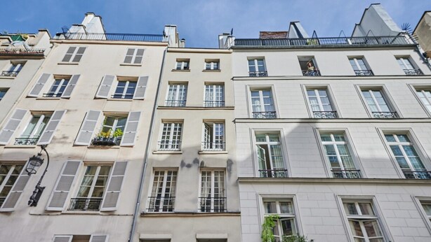 Una hilera de edificios de varios pisos con un estilo arquitectónico uniforme, con balcones y ventanas con persianas.