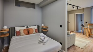 Un dormitorio moderno con cama, mesitas de noche, un ventanal y vistas a un comedor.