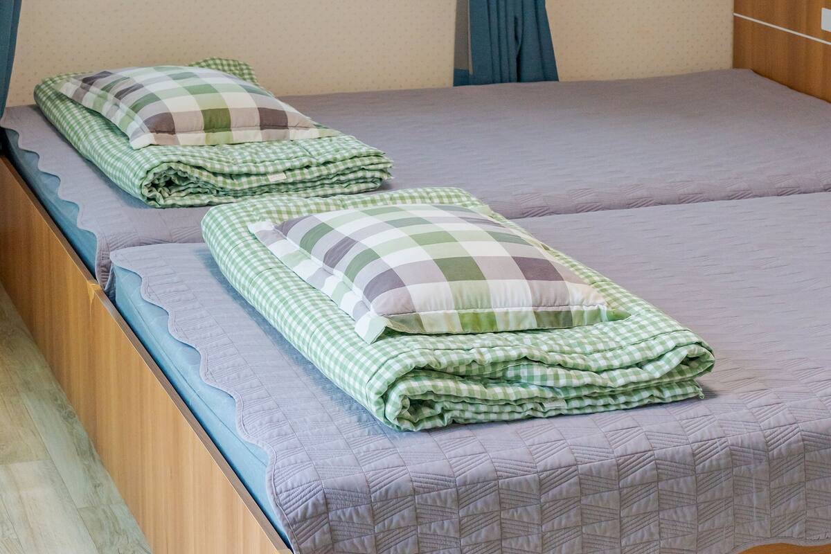 A double bed with a checkered bedspread and pillows, a wooden headboard, and a blue curtain.