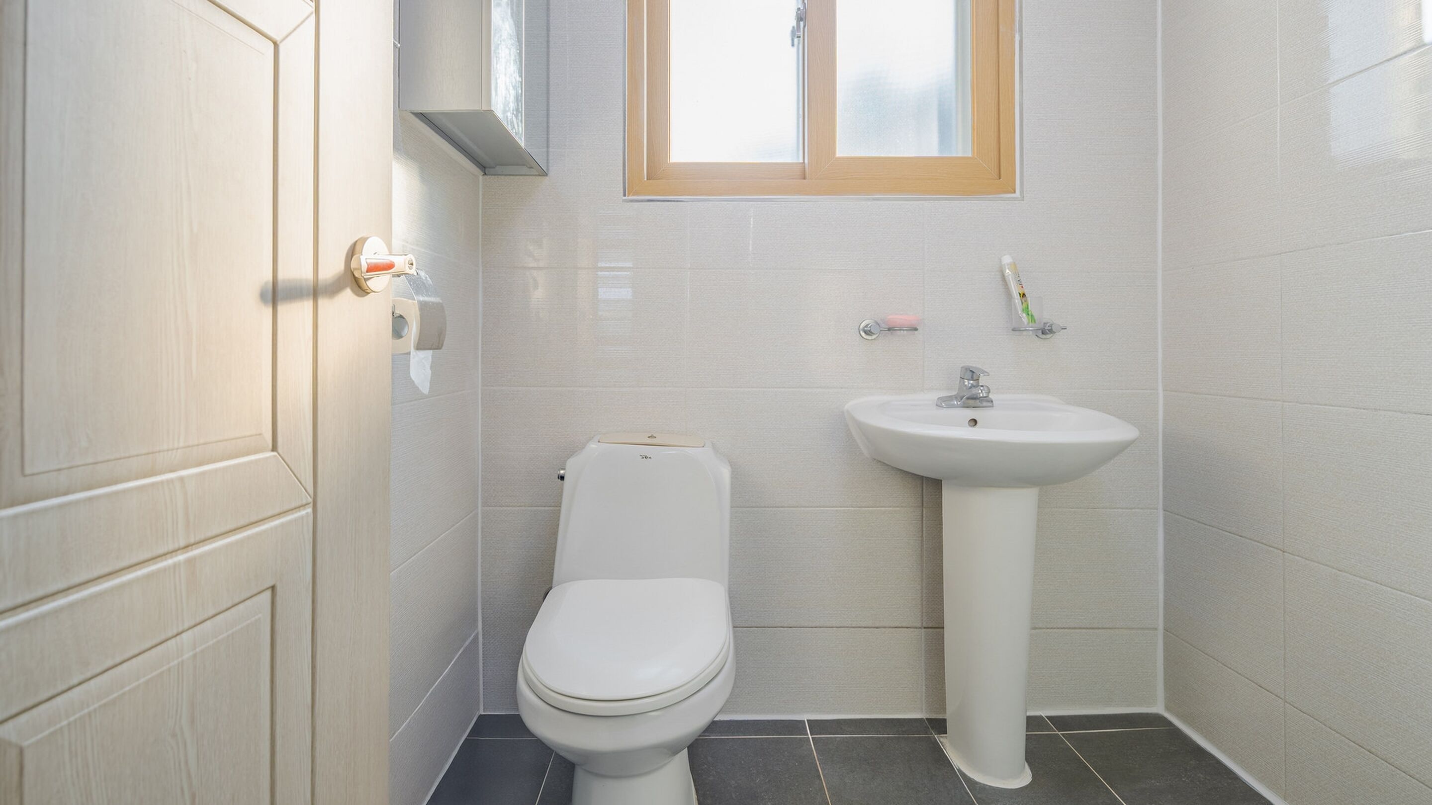 Une petite salle de bain propre, équipée de toilettes, d’un lavabo et d’une fenêtre située au-dessus du lavabo.