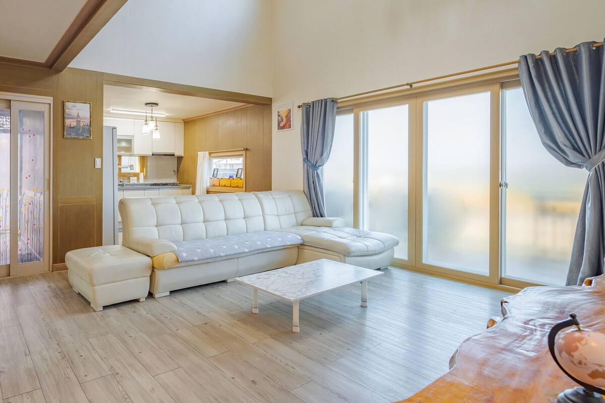 A spacious living room with a large sofa, a coffee table, and a view of the outdoors through large windows.