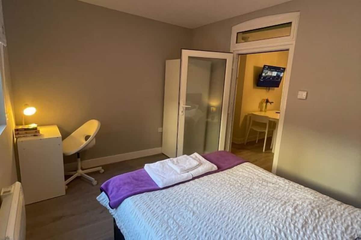 Ein Schlafzimmer mit Bett, Schreibtisch, Stuhl und Fernseher.