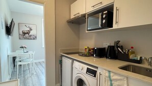 A compact kitchen with a washing machine, microwave, and a dining area with a table and chairs. - Chamberlayne Inn (London)