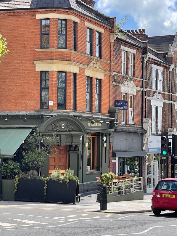 A traditional brick building with a corner entrance, a pub named "The Crumberlayne" with outdoor seating, and a visible street sign for "Wick." - Chamberlayne Inn (London)