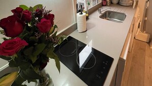 A kitchen with a modern stove, a glass vase with red roses, a window, and a shelf with kitchenware. - Chamberlayne Inn (London)
