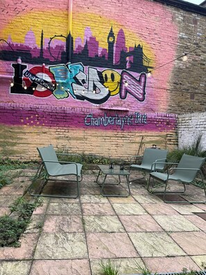 A mural of London on a brick wall with two metal chairs in front. - Chamberlayne Inn (London)