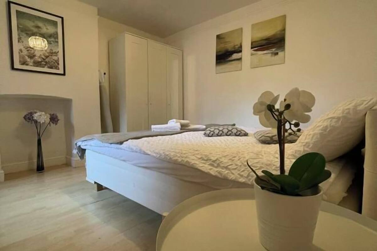 Ein Schlafzimmer mit einem Bett, einem Nachttisch mit Pflanze, einem Kleiderschrank und zwei Wandbildern.
