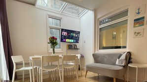 A modern living room with a grey sofa, white chairs, a small table, and a TV mounted on the wall. - Chamberlayne Inn (London)