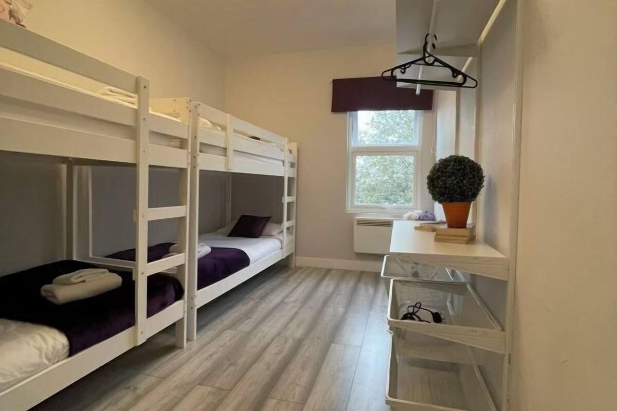 Ein Schlafraum mit Etagenbett, Fenster, Topfpflanze und Regal mit einem hängenden Gegenstand.