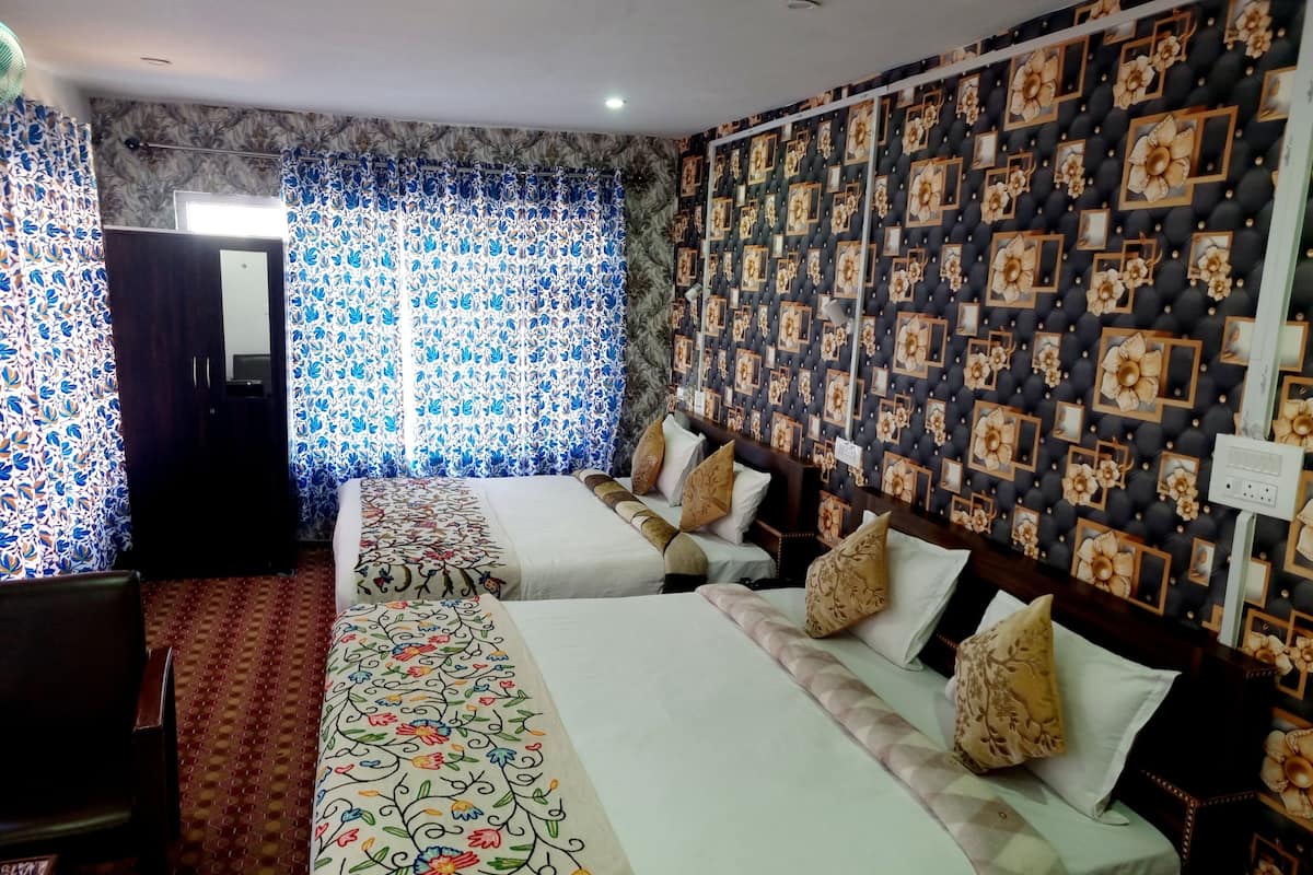 Una habitación de hotel con dos camas, cortinas florales, un papel tapiz estampado y suelo alfombrado.