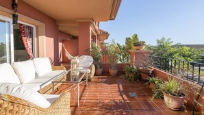 A balcony with a wicker sofa, a small table, potted plants, and a view of the landscape. - Spikes - Apartment In Sotogrande. Free Wifi (, Cádiz)