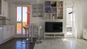 Una sala de estar moderna con televisor, muebles blancos y vistas al balcón.