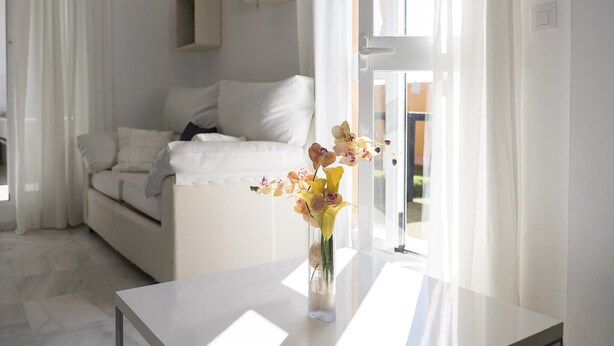 Un salón moderno con un sofá blanco, una mesa de centro de cristal y un jarrón con orquídeas.