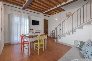 Un coin repas avec une table et des chaises en bois, un téléviseur fixé au mur et un escalier menant à l’étage supérieur.