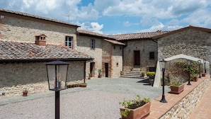 A courtyard with stone buildings, a covered walkway, and potted plants. - La Capanna, Borgo Campassini, Monteriggioni (Monteriggioni)