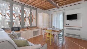 Un'ampia cucina con mobili bianchi, un tavolo da pranzo in legno e un televisore montato a parete.