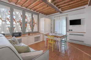 Une cuisine spacieuse avec des meubles blancs, une table à manger en bois et un téléviseur fixé au mur.