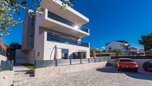 A modern two-story house with a balcony, a paved driveway, and a parked car. - Apartments Velic - apartment with terrace B (Šibenik-Brodarica)