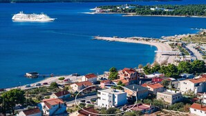 A coastal town with a cruise ship in the sea, buildings with red roofs, and a beach. - Apartments Velic - apartment with terrace B (Šibenik-Brodarica)