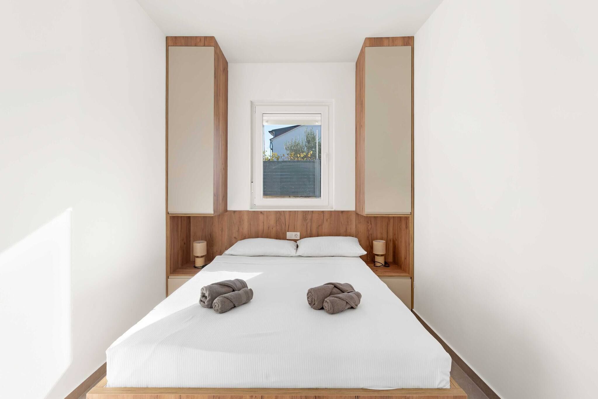 Une chambre à coucher avec un grand lit, deux tables de chevet, une fenêtre et une vue sur l’extérieur.