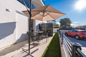 Relax in style on this outdoor patio with a metal table and chairs under a spacious umbrella, surrounded by a beautifully manicured lawn.