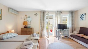 Quarto de hotel com duas camas, um sofá, uma televisão e uma mesa de vidro com vista para o exterior.