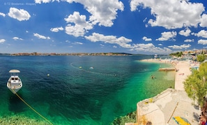Een kustgezicht met een boot die dichtbij de oever ligt, helder turquoise water en een strand met mensen en ligbedden.
