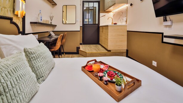A hotel room with a bed, a tray with breakfast items, a desk with a chair, a TV, and a bathroom with a mirror and shelves. - WS - Opéra - Milan (Paris)