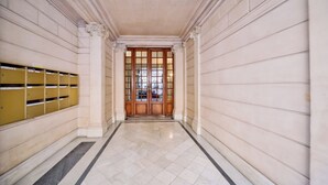 A hallway with a marble floor, wooden doors, and a yellow locker area. - WS - Opéra - Milan (Paris)