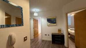A hotel room with a wooden floor, a bedside table, a bed, a painting on the wall, and a telephone on the wall. - Cosy City Centre Apartment with parking (West Midlands)