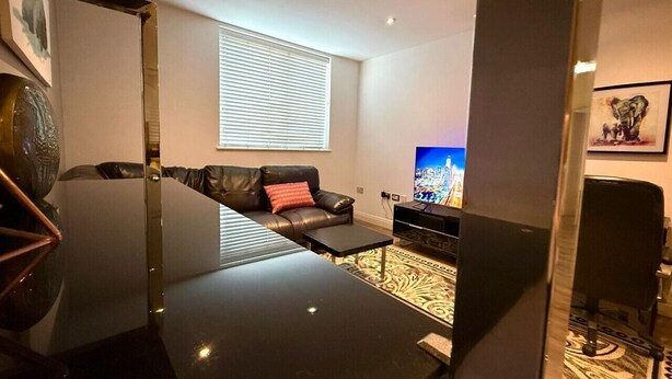 A modern living room with a black leather sofa, a small coffee table, and a flat-screen TV. - Cosy City Centre Apartment with parking (West Midlands)